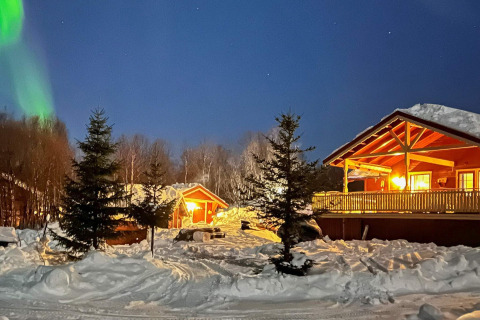 Sneeuwchalet in Jarfjord, Zweden, sfeervol verlicht met noorderlicht en dennenbomen ’s nachts.