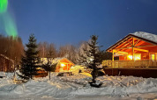 Sneeuwchalet in Jarfjord, Zweden, sfeervol verlicht met noorderlicht en dennenbomen ’s nachts.