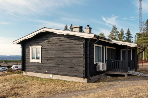 Chalet de vacances noir avec toit blanc à Kopparberg, Suède, entouré de forêts et de paysage vallonné.