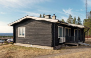 Chalet de vacances noir avec toit blanc à Kopparberg, Suède, entouré de forêts et de paysage vallonné.