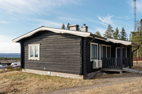 Zwart houten vakantiehuis met wit dak in Kopparberg, Zweden, gelegen nabij bos en heuvelachtig landschap.