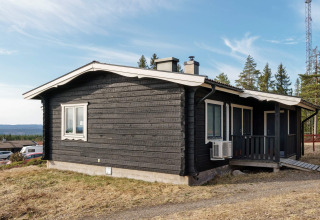 Zwart houten vakantiehuis met wit dak in Kopparberg, Zweden, gelegen nabij bos en heuvelachtig landschap.