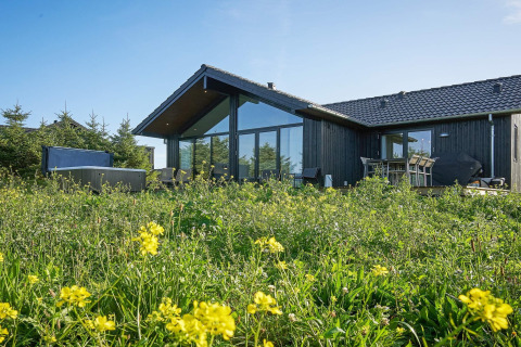 Moderne vakantiewoning voor 8 personen in Aakirkeby, omgeven door bloemen en groen, met grote ramen.