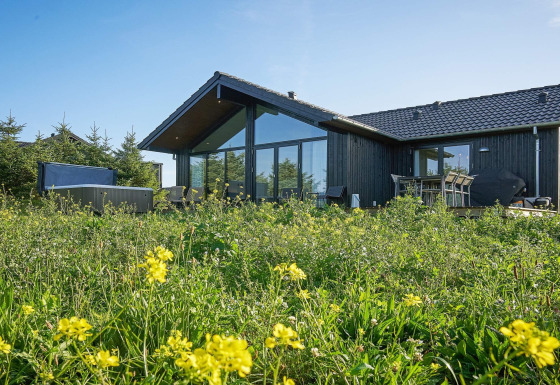Casa de vacaciones para 8 personas en Aakirkeby, rodeada de flores silvestres y naturaleza, con ventanales.