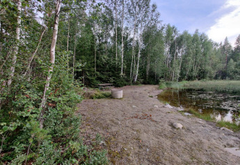 Bosrijk tafereel met meer, picknicktafel en vuurcirkel bij vakantiewoning in Kopparberg, Zweden.