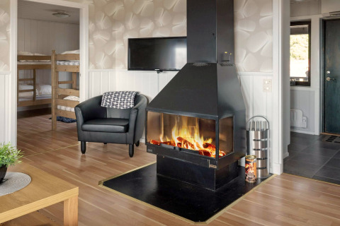Salon d’une maison de vacances à Kopparberg, Suède, avec cheminée, fauteuil, TV et lits superposés.