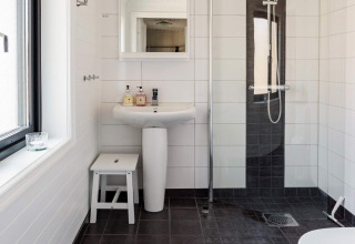 Moderne badkamer in een vakantiehuis in Kopparberg, Zweden, met douche, wastafel en witte inrichting.