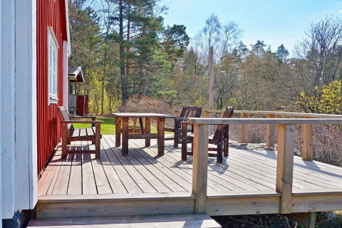 Terrazza in legno con tavolo e sedie accanto a uno chalet rosso, immersa tra alberi, a Vaxholm, Svezia.