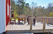 Terrasse en bois avec table et chaises devant un chalet rouge, entourée d’arbres, à Vaxholm, Suède.