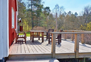 Terrazza in legno con tavolo e sedie accanto a uno chalet rosso, immersa tra alberi, a Vaxholm, Svezia.