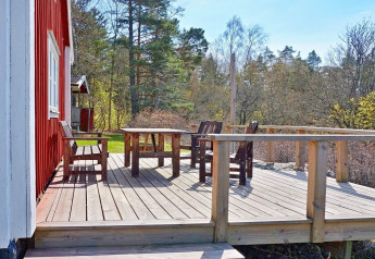 Holzterrasse mit Tisch und Stühlen an rotem Haus, umgeben von Bäumen, im 6-Personen-Ferienhaus in Vaxholm, Schweden.