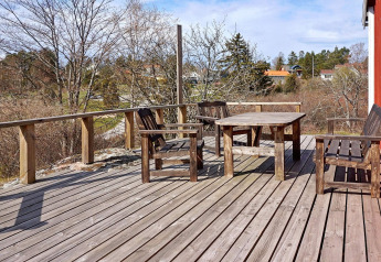 Terraza de madera con muebles rústicos al aire libre en una cabaña en Vaxholm, Suecia, rodeada de naturaleza.