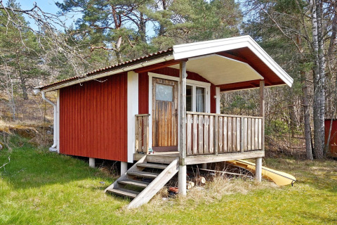 Chalet in legno rosso con veranda a VAXHOLM, Svezia, casa vacanze per 6 persone immersa tra alberi.
