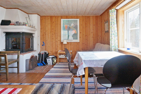 Accogliente soggiorno in chalet svedese a Vaxholm, con pareti in legno, camino, tavolo da pranzo e tappeti.