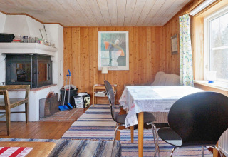 Accogliente soggiorno in chalet svedese a Vaxholm, con pareti in legno, camino, tavolo da pranzo e tappeti.