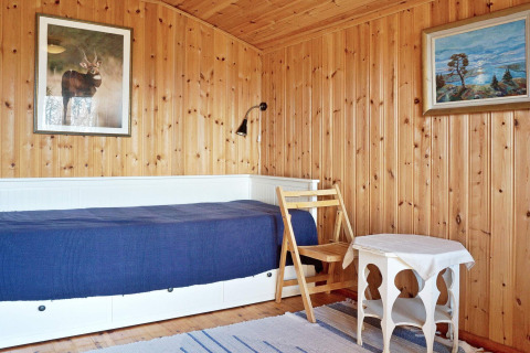 Camera in chalet a Vaxholm, Svezia, con pareti in legno, letto singolo, sedia, tavolino e quadri.