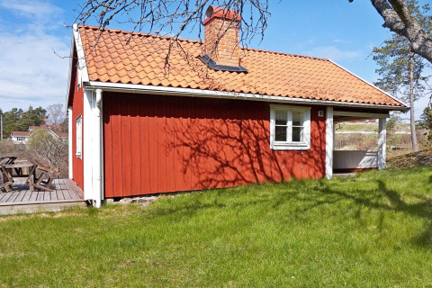 Chalet rosso con tetto in tegole e terrazza in legno a Vaxholm, Svezia, circondato dal verde.