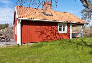 Chalet rosso con tetto in tegole e terrazza in legno a Vaxholm, Svezia, circondato dal verde.