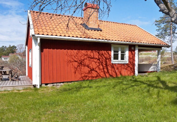 Rotes Ferienhaus mit Ziegeldach und Terrasse im Grünen in Vaxholm, Schweden, bei Sonnenschein.