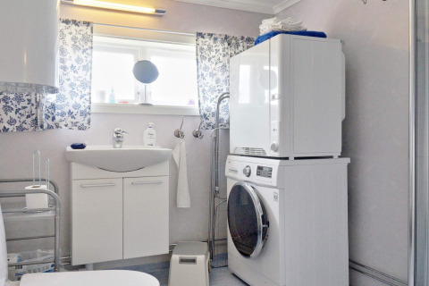 Bagno luminoso in una casa vacanze a Vaxholm, Svezia, con lavatrice, asciugatrice e tende floreali azzurre.