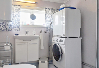 Helles Badezimmer in einem Ferienhaus in Vaxholm, Schweden, mit Waschmaschine, Trockner und Blumenvorhängen.