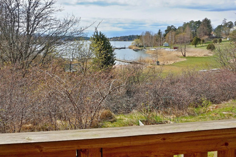 Vista da una terrazza in legno su lago tranquillo, pontili e prati verdi a Vaxholm, Svezia.