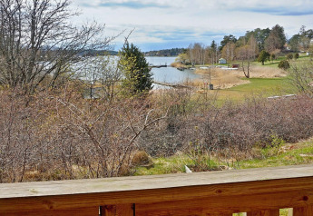 Udsigt fra træterrasse over en rolig sø med bådebroer og grønne områder i Vaxholm, Sverige.