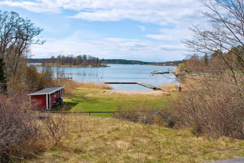 Vista lago e spiaggia con pontile da una casa vacanze per 6 persone a Vaxholm, Svezia, con casetta rossa.