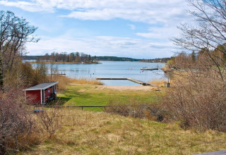 Vista lago e spiaggia con pontile da una casa vacanze per 6 persone a Vaxholm, Svezia, con casetta rossa.