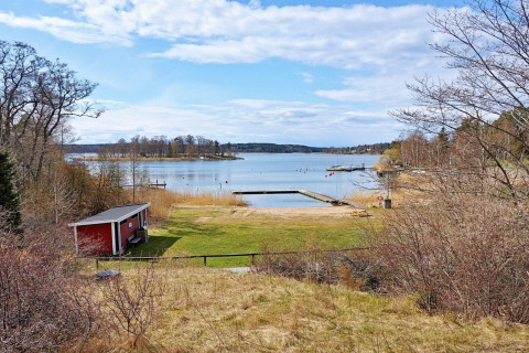 Vista dalla casa vacanze a Vaxholm, Svezia, con casetta rossa, prato verde, lago e molo in legno.