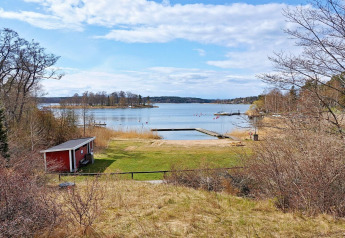 Uitzicht vanop het vakantiehuis in Vaxholm, Zweden met rood huisje, zwemsteiger en uitgestrekt meer.