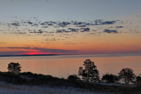 Zonsondergang boven zee met bomen en wolken, gezien vanaf het 6-persoons vakantiehuis in Børkop, Denemarken.