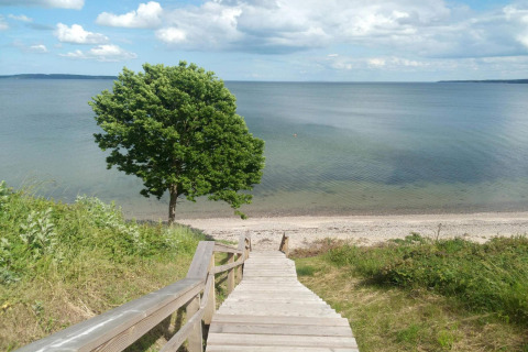 Houten trap leidt naar een strand bij het vakantiehuis in Børkop, Denemarken, onder een blauwe lucht.