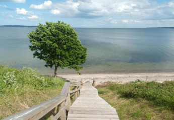 Escalier en bois descendant vers la plage près d'une maison de vacances à Børkop, Danemark, ciel bleu.