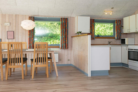 Lichte eetkamer en keuken met houten meubels in een vakantiehuis in Børkop, Denemarken, met grote ramen.