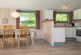 Lichte eetkamer en keuken met houten meubels in een vakantiehuis in Børkop, Denemarken, met grote ramen.
