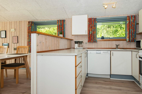 Lichte houten keuken met eethoek, vaatwasser en kleurrijke gordijnen in vakantiehuis in Børkop, Denemarken.