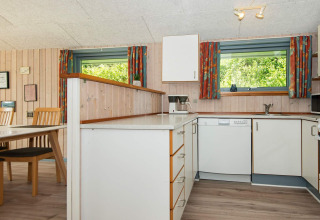Lichte houten keuken met eethoek, vaatwasser en kleurrijke gordijnen in vakantiehuis in Børkop, Denemarken.