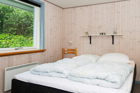 Slaapkamer met tweepersoonsbed, houten panelen, groot raam en plank in een vakantiehuis in Børkop.