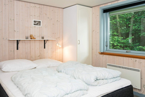 Slaapkamer met tweepersoonsbed, wit beddengoed, kledingkast en groot raam in vakantiehuis in Børkop, Denemarken.