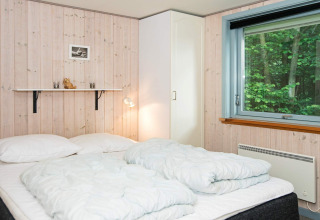 Slaapkamer met tweepersoonsbed, wit beddengoed, kledingkast en groot raam in vakantiehuis in Børkop, Denemarken.