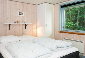 Slaapkamer met tweepersoonsbed, wit beddengoed, kledingkast en groot raam in vakantiehuis in Børkop, Denemarken.