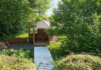 Houten prieel met overdekt terras en pad bij 6-persoons vakantiewoning in Børkop, Denemarken, omgeven door groen.