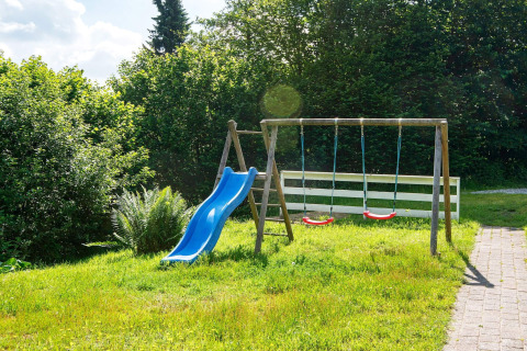Speelplaats met blauwe glijbaan en schommels op grasveld bij 6-persoons vakantiewoning in Børkop, Denemarken.