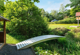 Houten brug over een beekje in de tuin van een vakantiehuis in Børkop, Denemarken, met veel groen.