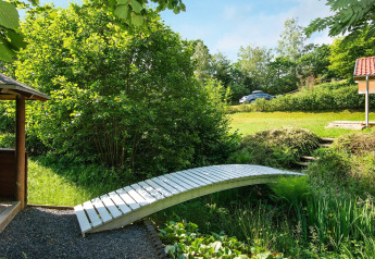 Houten brug over een beekje in de tuin van een vakantiehuis in Børkop, Denemarken, met veel groen.