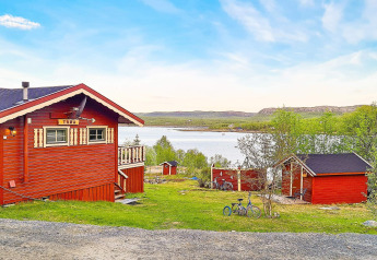 Rød hytte ved en sø med cykler og grønne træer omkring, taget i Jarfjord, Sverige, på en solrig dag.