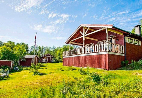 Chalet in Jarfjord voor 7 personen, rood geschilderd, omgeven door gras en onder een blauwe lucht.