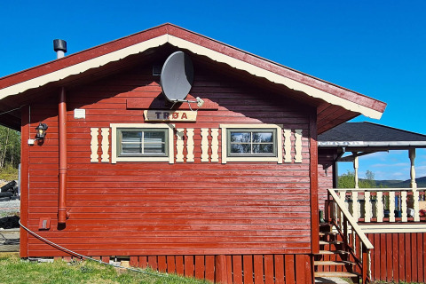 Rotes Holzchalet mit Satellitenschüssel, Schildern und Veranda bei blauem Himmel in Jarfjord, Schweden.
