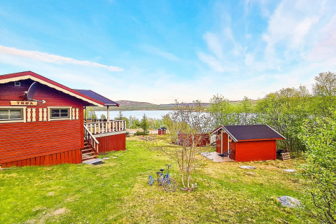 Rood chalet aan het meer in Jarfjord, Zweden, omringd door groen en een fiets op het gras.